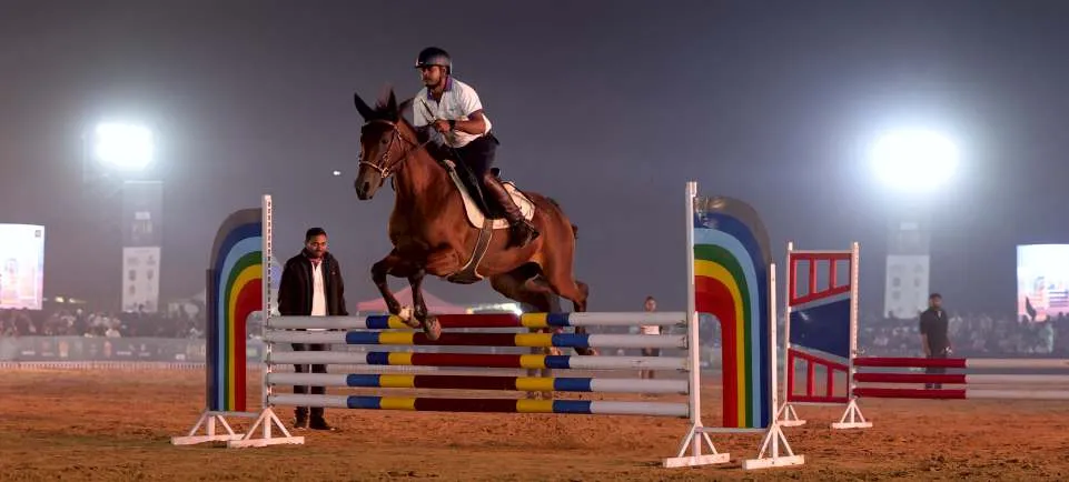 A rider clears a show-jumping fence under floodlights