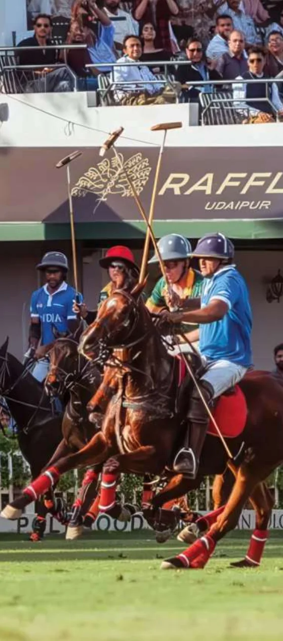 Polo players in red and blue jerseys contesting the ball before a packed stand